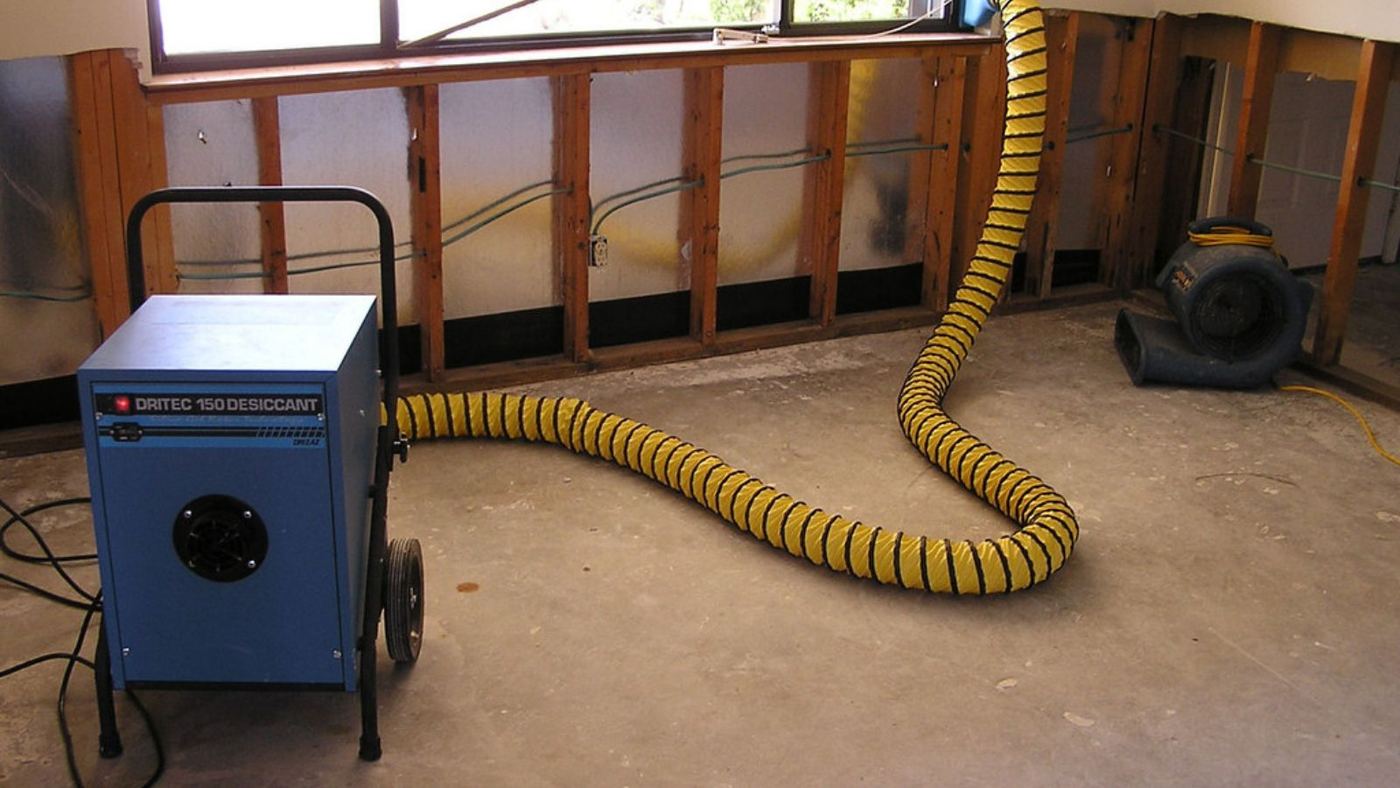 Dehumidifier with a yellow duct drying a room with open wall cavities